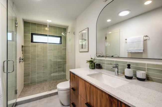 Modern bathroom with wood vanity, green tile shower, and glass enclosure in Sacramento by MAK Design + Build